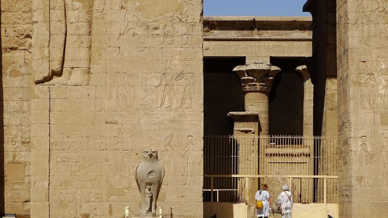Sunlit façade of an ancient Egyptian temple featuring intricate hieroglyphs and sculptures.