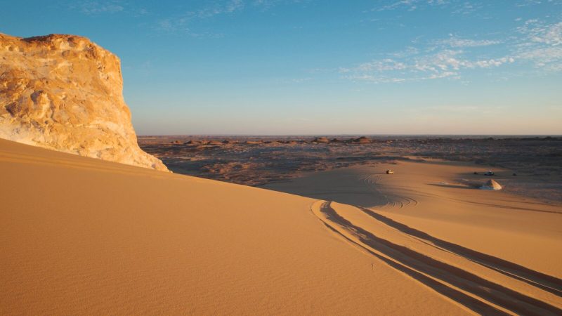 Stunning view of golden desert dunes under a clear blue sky, captured during sunset.