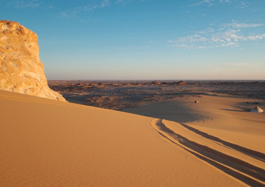 Stunning view of golden desert dunes under a clear blue sky, captured during sunset.