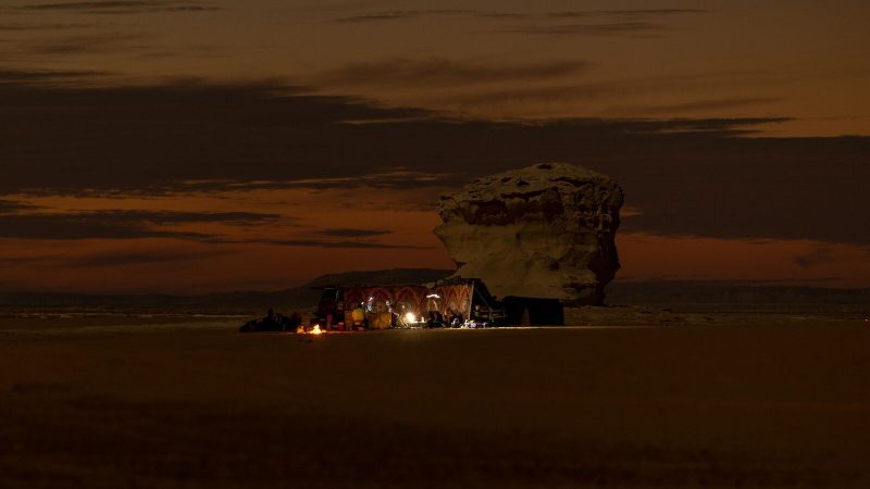 Nighttime campfire in Siwa Oasis, Egypt, with a rock formation and warm desert scenery.
