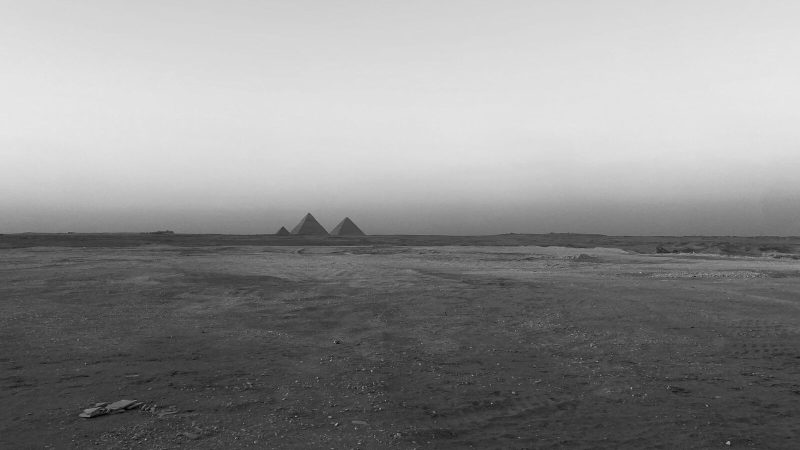 Black and white photo of pyramids in Egypt's arid landscape showing vast desert scenery.