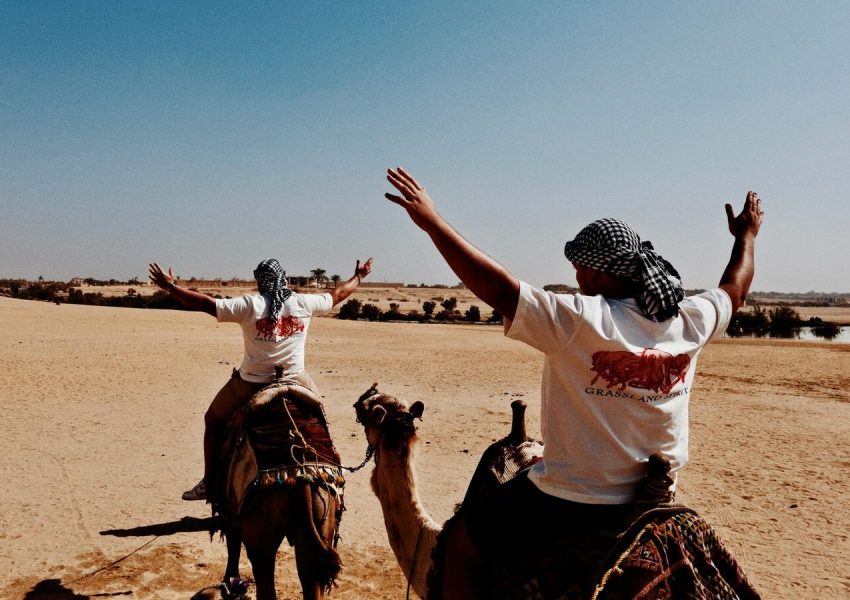 Men riding camels in the expansive Oasi del Fayyum desert, Egypt.