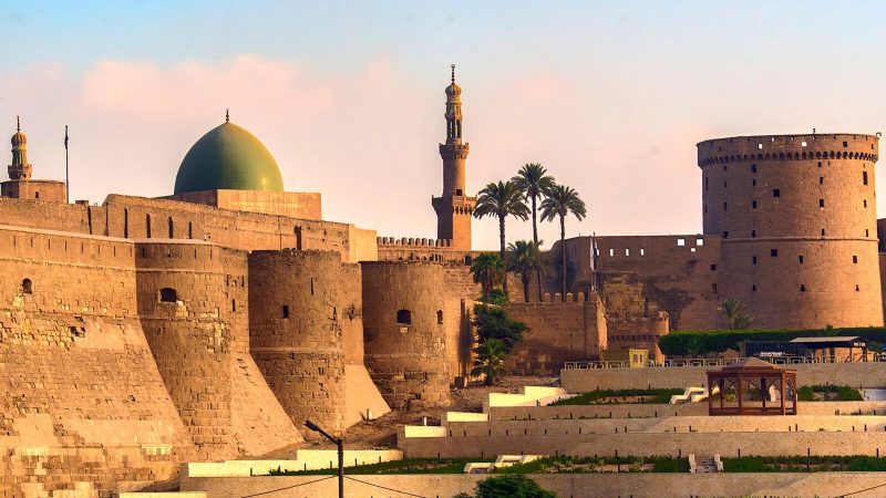 Ancient citadel with minarets and dome in a sunny cityscape setting, showcasing rich architecture.