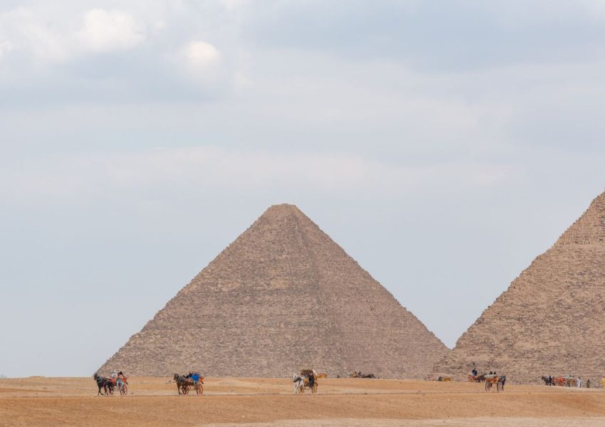 Camel riders near the iconic pyramids of Giza under a cloudy sky, showcasing Egypt's historical allure.