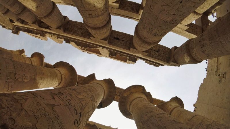 Upward view of ancient columns at Karnak Temple, showcasing intricate hieroglyphics.