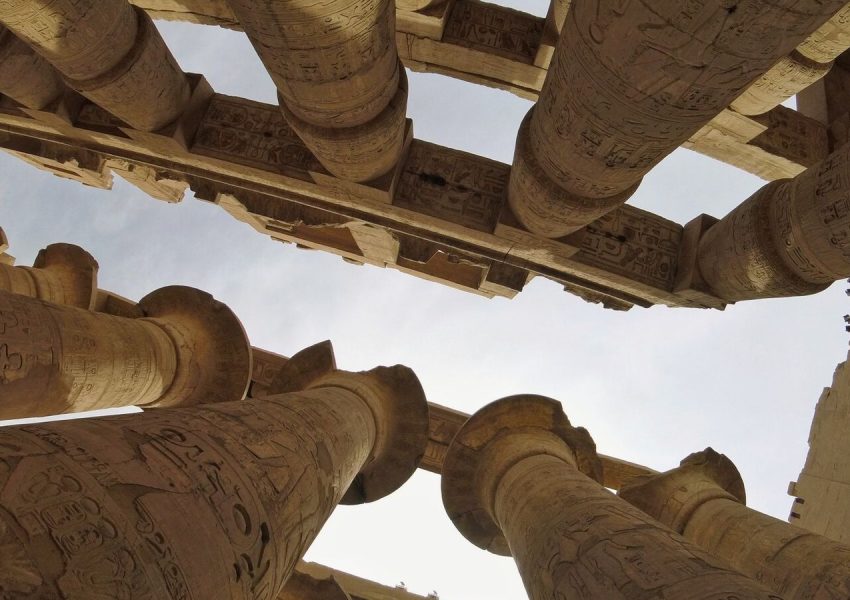 Upward view of ancient columns at Karnak Temple, showcasing intricate hieroglyphics.