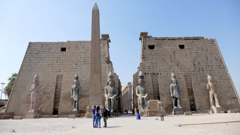 Visitors explore the iconic entrance of Luxor Temple, featuring colossal statues and an obelisk.