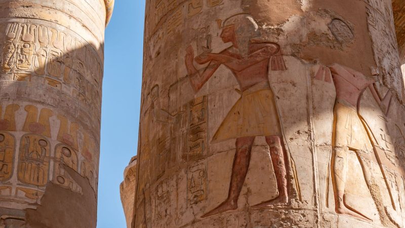 Close-up of ancient Egyptian temple columns with hieroglyphs and carvings under bright sunlight.