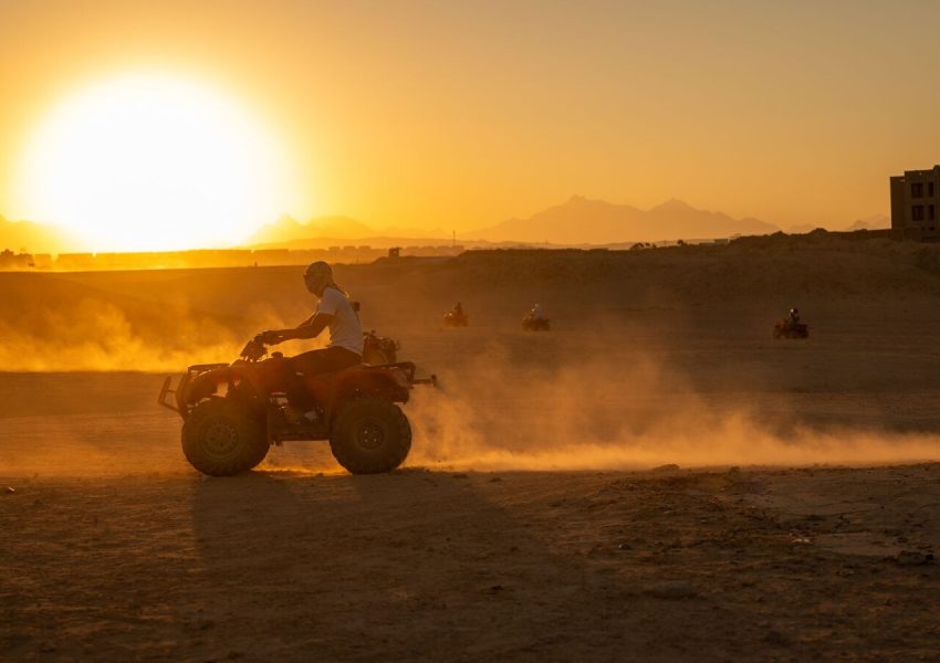 ATV riders explore the desert landscape at sunset, creating a scene filled with dust and motion.