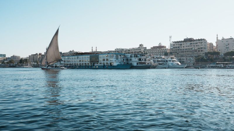 A picturesque view of a traditional sailboat on the Nile River near city waterfronts.