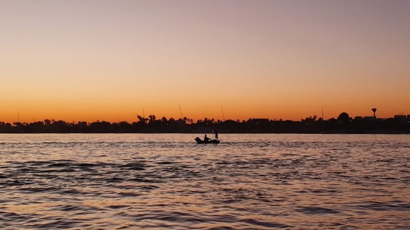 Peaceful boat silhouette on the Nile at sunset, capturing the tranquil Egyptian landscape.
