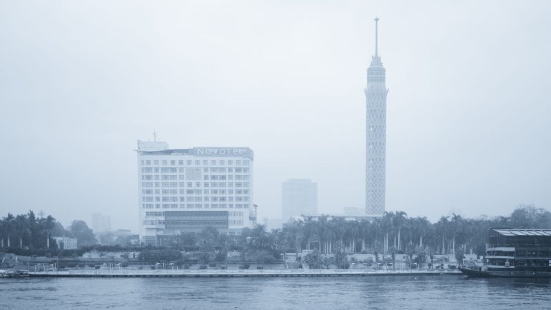 Foggy cityscape of Cairo featuring the Cairo Tower and Novotel by the Nile River.