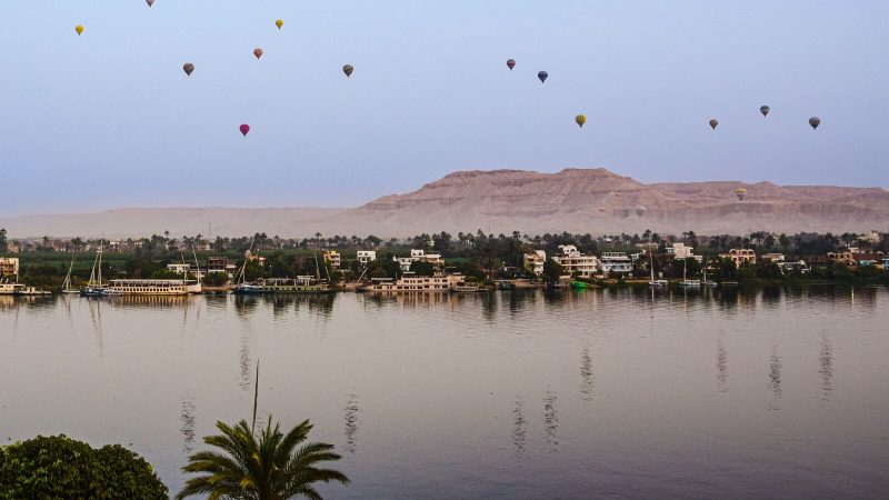 Scenic view of hot air balloons floating over the Nile River near Egyptian desert at dusk.