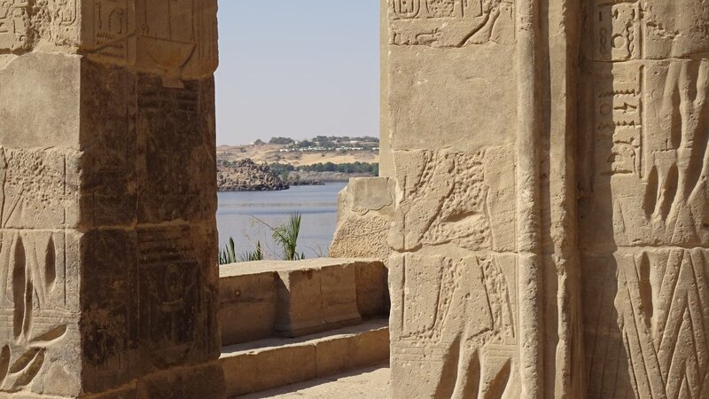Stone ruins of an Egyptian temple adorned with hieroglyphs by the Nile River under clear skies.