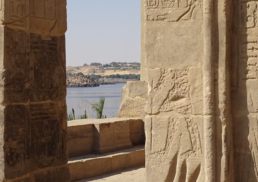 Stone ruins of an Egyptian temple adorned with hieroglyphs by the Nile River under clear skies.