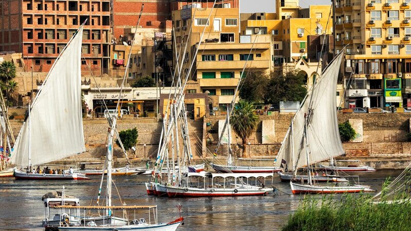 Vibrant Aswan riverfront with traditional feluccas sailing on the Nile.