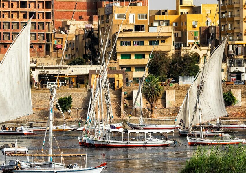 Vibrant Aswan riverfront with traditional feluccas sailing on the Nile.