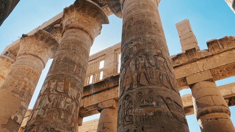Impressive ancient Egyptian temple columns with hieroglyphics under a clear blue sky.