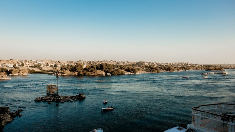 A picturesque view of Aswan's Nile River with boats and lush shoreline under a clear blue sky.