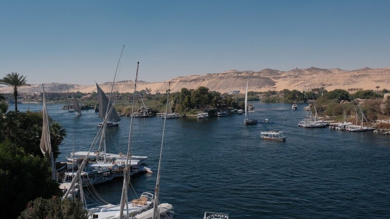 Steamboats and sailboats navigate the scenic Nile River with desert hills in the background, Egypt.