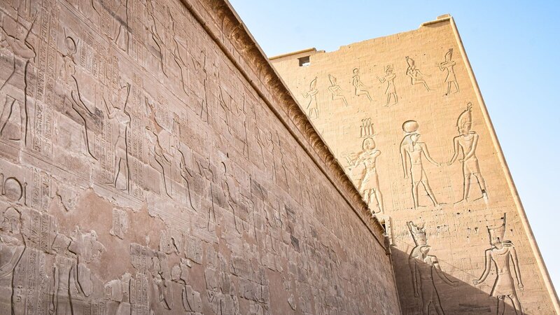Detailed view of ancient Egyptian temple walls featuring hieroglyphs and historical depictions under clear blue skies.
