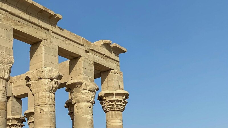 Stone columns of an ancient Egyptian temple under a clear blue sky in Aswan, Egypt.