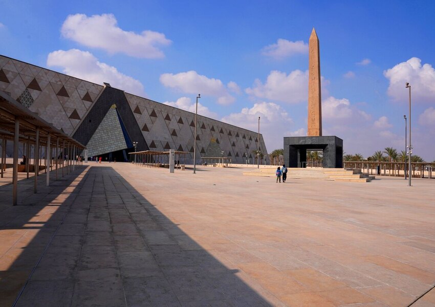 Wide-angle view of the Grand Egyptian Museum with a prominent obelisk and clear skies.