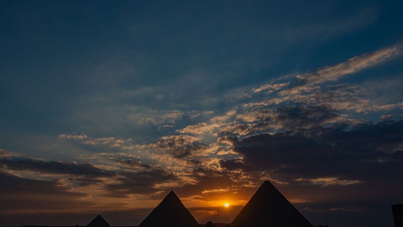Silhouette of Giza pyramids against a dramatic sunset sky.