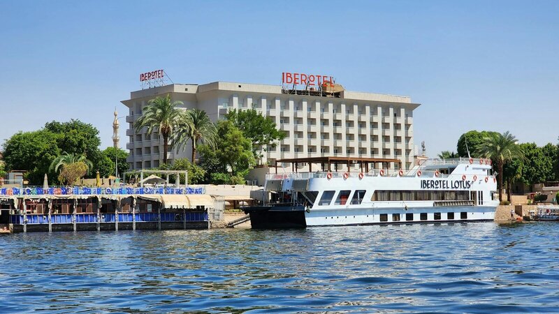Scenic view of Hotel Iberotel by the Nile River with a cruise boat docked nearby.
