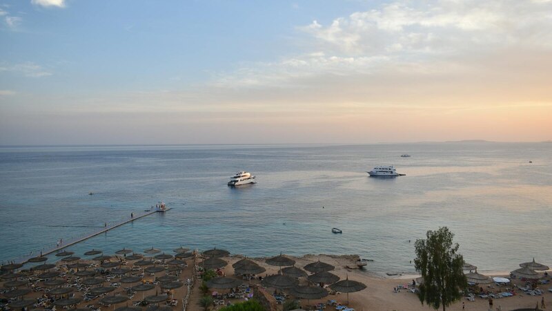 Stunning aerial view of Sharm El Sheikh's beach and sea during sunset with boats and parasols.