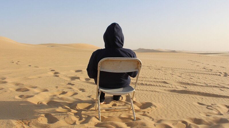 A lone person sits on a chair in the vast Siwa Oasis desert dunes, Egypt.