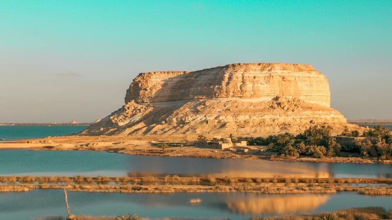 Eroded rock formation by a tranquil lake in a desert landscape, perfect for nature and travel photography.