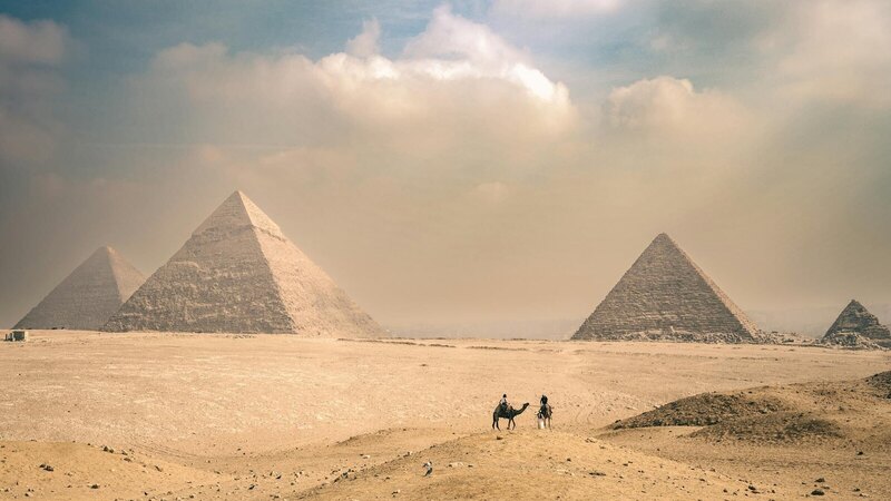 Explore the majestic Pyramids of Giza under a sunny sky with distant travelers on camels.