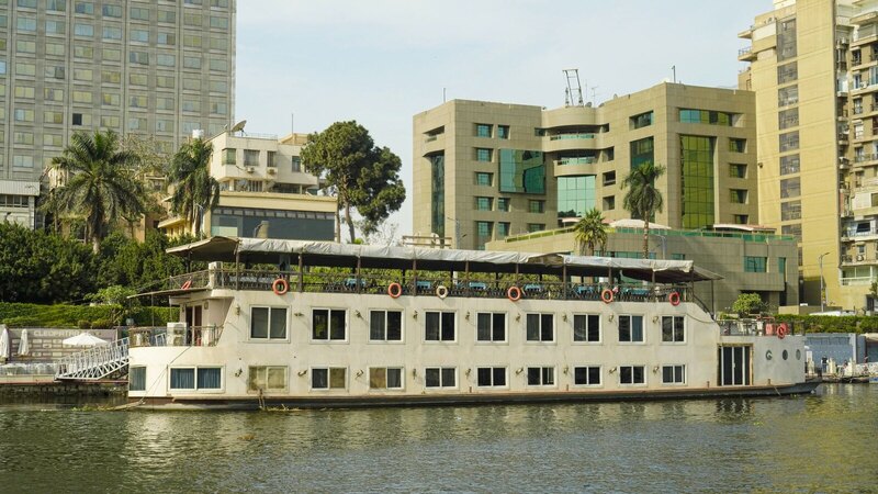 A serene scene of a cruise boat on the Nile River in Cairo, Egypt, with modern buildings in the background.
