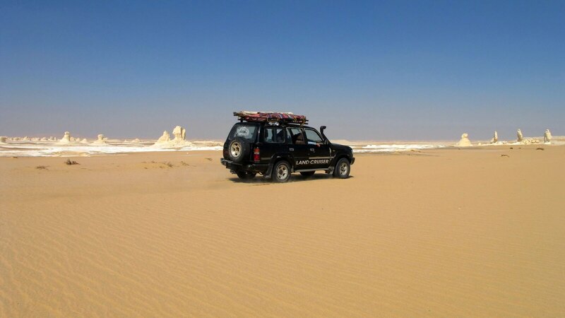 Explore the vast Egyptian White Desert with a 4x4 vehicle under a clear blue sky.