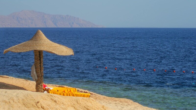 Serene beach with a straw parasol, sandy shore, and clear blue sea under a sunny sky.