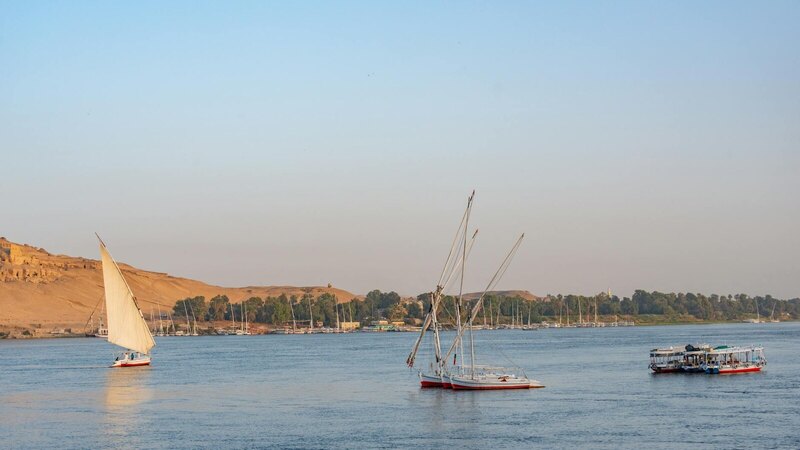 Classic sailboats glide along the Nile with a scenic backdrop of Aswan's desert landscape.