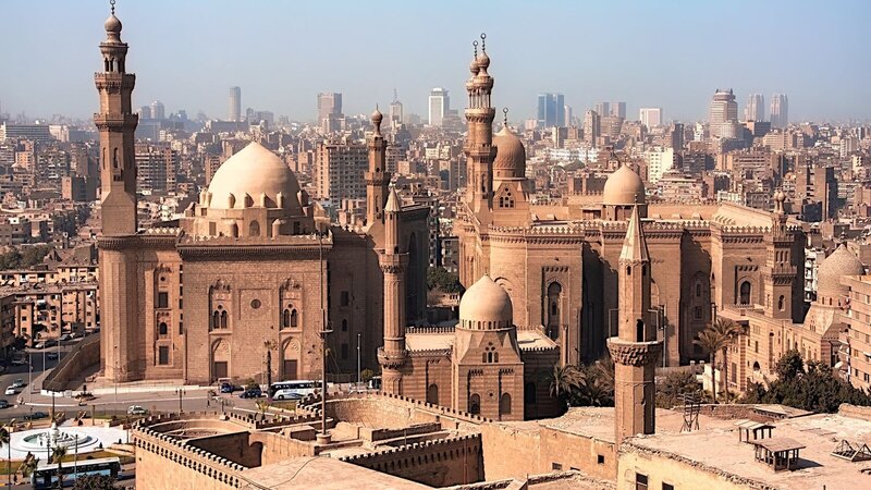 Aerial view of historic mosques with Cairo cityscape backdrop, showcasing Islamic architecture.
