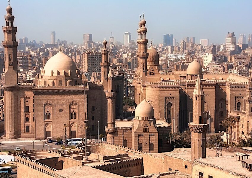 Aerial view of historic mosques with Cairo cityscape backdrop, showcasing Islamic architecture.