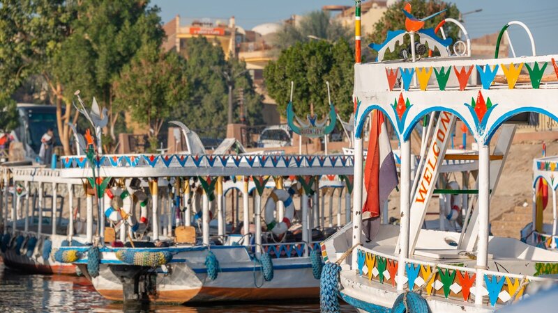 Vibrant traditional boats docked at Aswan harbor in Egypt, showcasing colorful designs and a lively atmosphere.