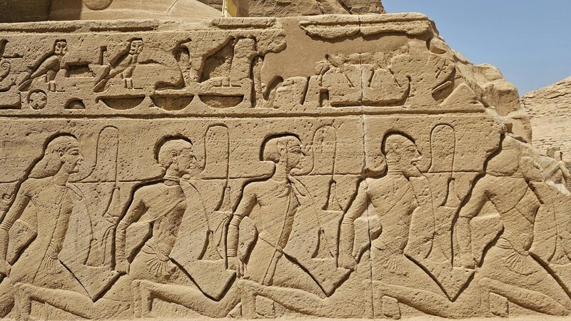 Detailed view of ancient Egyptian hieroglyphs carved on a stone wall under sunny skies.