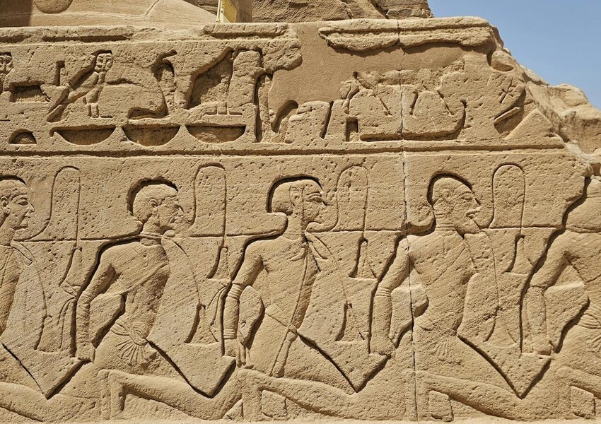 Detailed view of ancient Egyptian hieroglyphs carved on a stone wall under sunny skies.