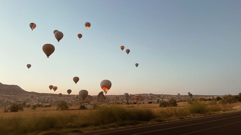 Scenic view of hot air balloons floating over the Cappadocia landscape at sunrise in Türkiye.