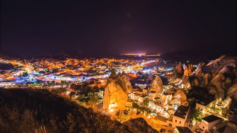 A vibrant nighttime aerial view of Göreme National Park with illuminated landmarks in Cappadocia, Turkey.